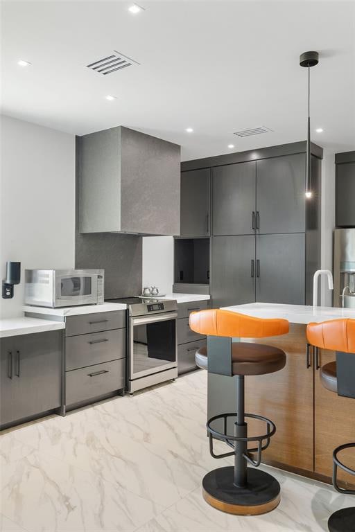 kitchen featuring gray cabinetry, decorative light fixtures, wall chimney range hood, and appliances with stainless steel finishes