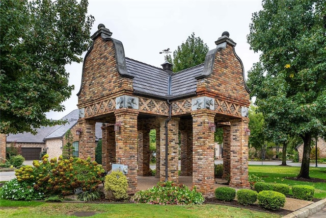 view of front facade featuring brick siding, a chimney, a front lawn, and a gambrel roof