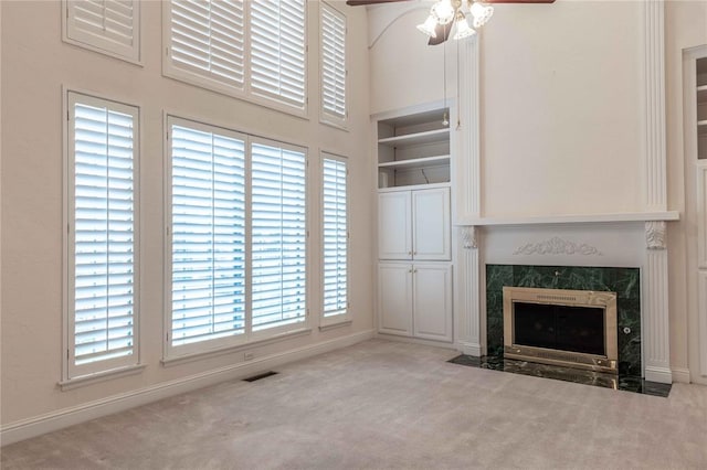 unfurnished living room with a ceiling fan, light carpet, a towering ceiling, and a premium fireplace