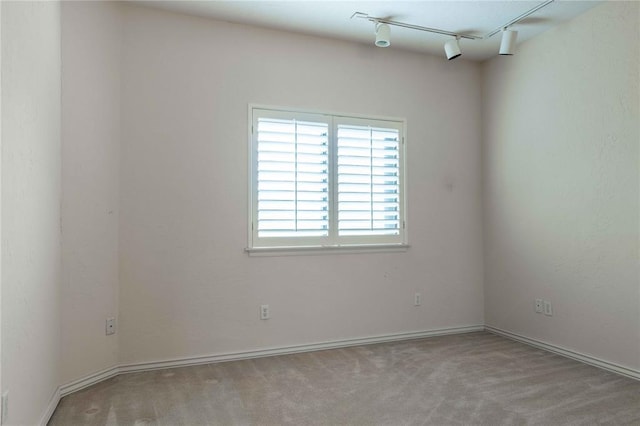 spare room featuring light carpet, rail lighting, and baseboards