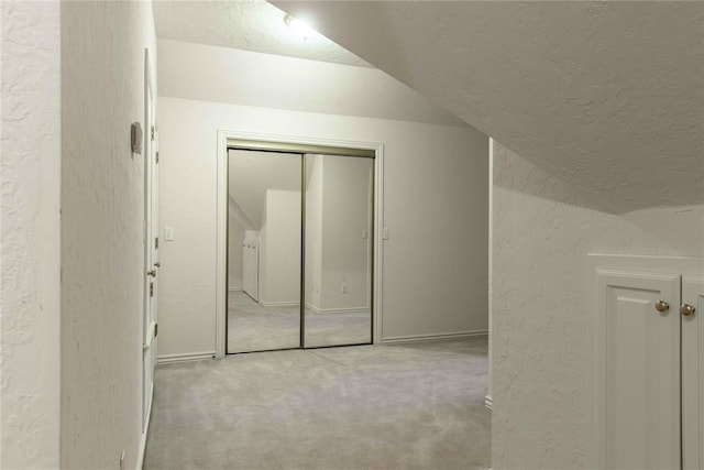 bonus room with vaulted ceiling, a textured wall, a textured ceiling, and light colored carpet