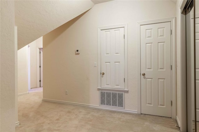 additional living space featuring light colored carpet, visible vents, a textured wall, and lofted ceiling