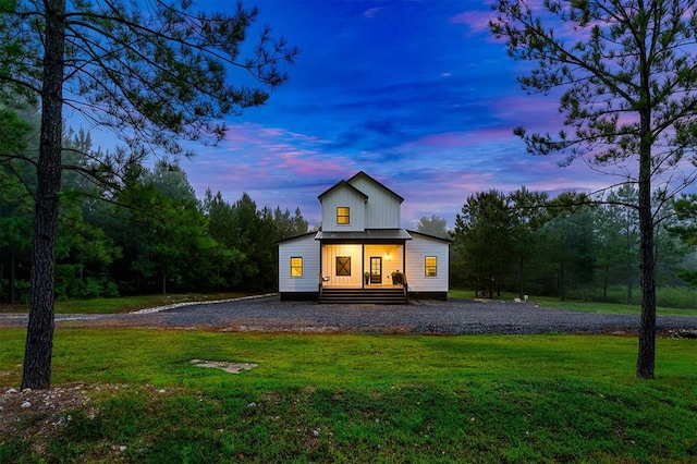 back house at dusk with covered porch and a lawn