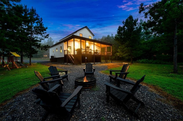 back house at dusk featuring a playground, a sunroom, a yard, and a fire pit