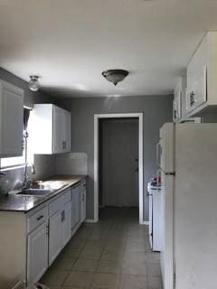 kitchen with white cabinetry, sink, dark tile patterned flooring, and white appliances