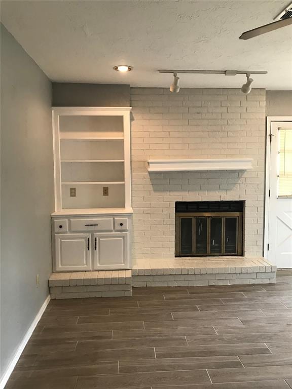 unfurnished living room featuring a fireplace, track lighting, and dark wood-type flooring