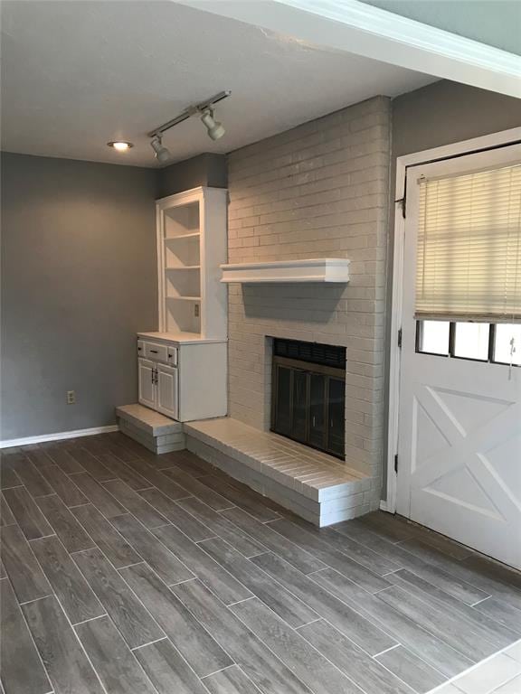 unfurnished living room featuring a fireplace, rail lighting, and hardwood / wood-style flooring