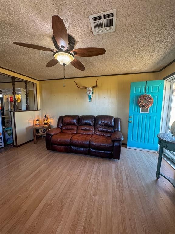 living room with hardwood / wood-style floors, a textured ceiling, ceiling fan, and wooden walls