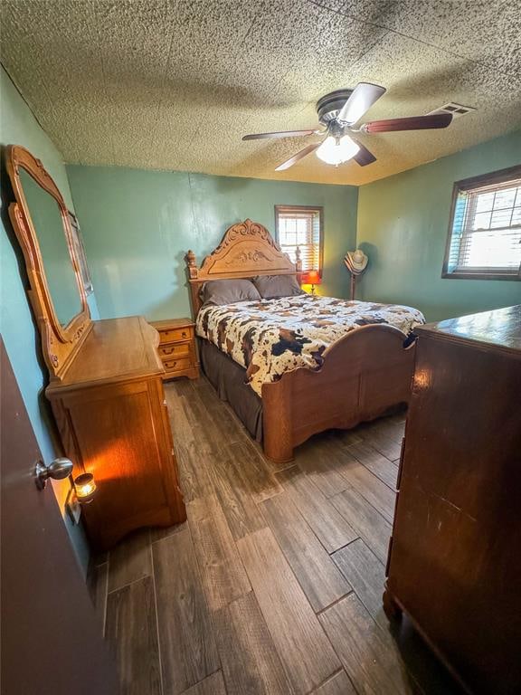 bedroom featuring multiple windows, hardwood / wood-style floors, a textured ceiling, and ceiling fan