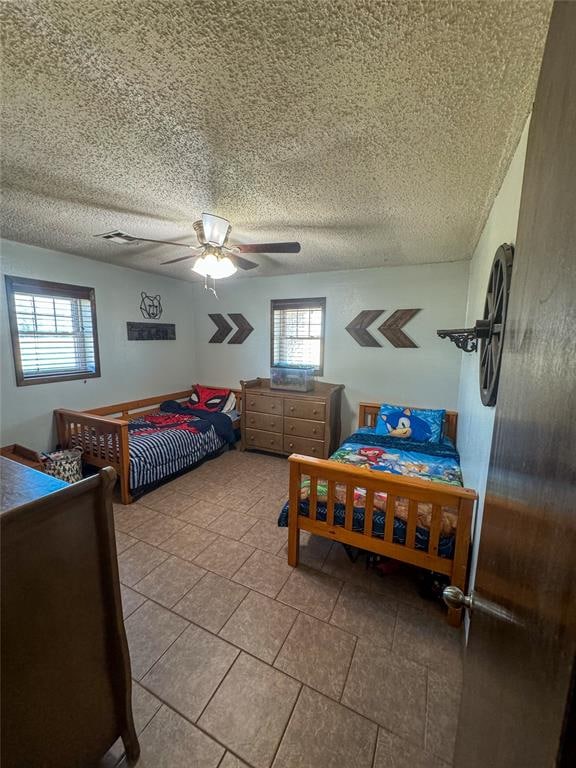 bedroom featuring ceiling fan, light tile patterned floors, and a textured ceiling