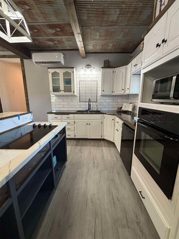 kitchen with white cabinetry, sink, a wall mounted AC, light hardwood / wood-style floors, and black appliances