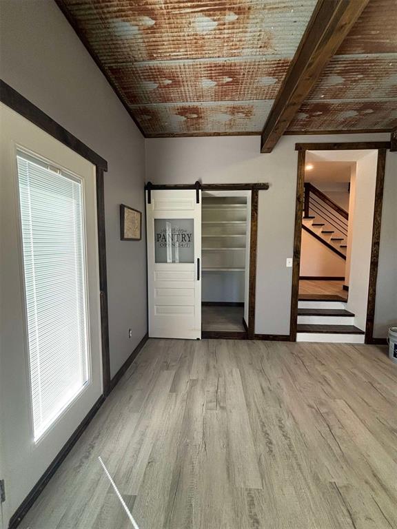 interior space featuring beam ceiling, a barn door, light hardwood / wood-style flooring, and multiple windows