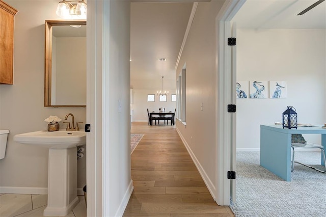 hallway with a sink, light wood-style flooring, baseboards, and an inviting chandelier