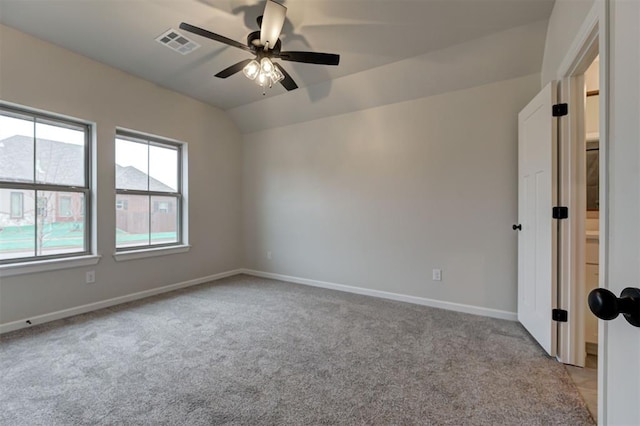 empty room featuring lofted ceiling, light colored carpet, visible vents, a ceiling fan, and baseboards