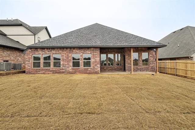 rear view of property featuring a shingled roof, fence, central AC, and brick siding