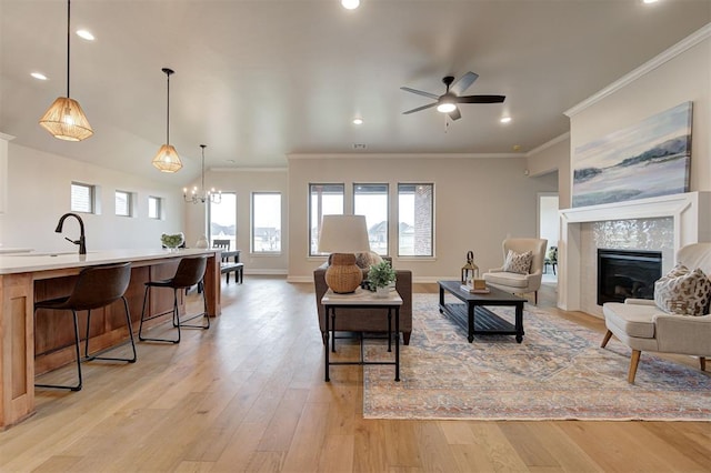 living area with ceiling fan with notable chandelier, a fireplace, baseboards, light wood finished floors, and crown molding