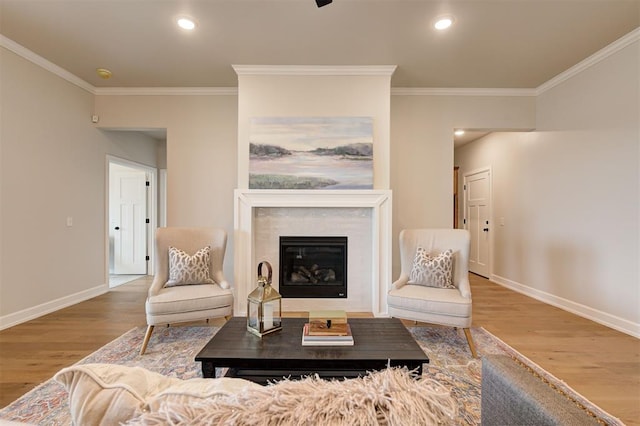 living area with a glass covered fireplace, crown molding, baseboards, and wood finished floors