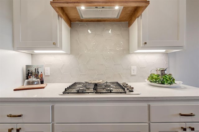 kitchen featuring tasteful backsplash, premium range hood, white cabinetry, and stainless steel gas stovetop