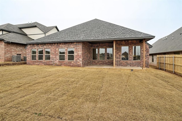 rear view of property featuring brick siding, fence, central AC, and roof with shingles