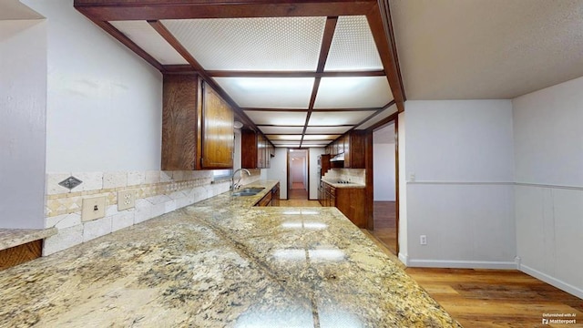 interior space with sink, light stone counters, tasteful backsplash, and light hardwood / wood-style floors