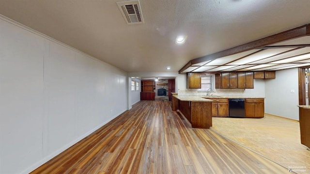 kitchen with beam ceiling, a stone fireplace, light hardwood / wood-style floors, black dishwasher, and kitchen peninsula