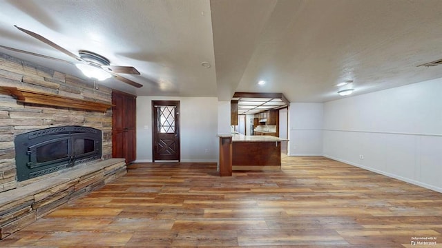 interior space featuring hardwood / wood-style floors, ceiling fan, and a stone fireplace