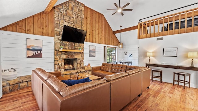 living room with ceiling fan, wooden walls, light hardwood / wood-style flooring, high vaulted ceiling, and a fireplace