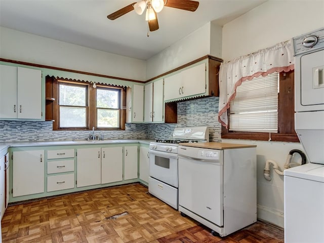 kitchen with sink, light parquet floors, stacked washer / drying machine, white appliances, and white cabinets