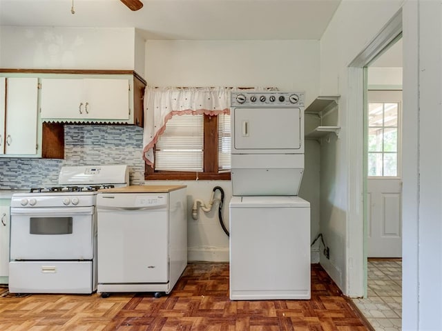 kitchen with white appliances, parquet flooring, stacked washing maching and dryer, tasteful backsplash, and white cabinetry