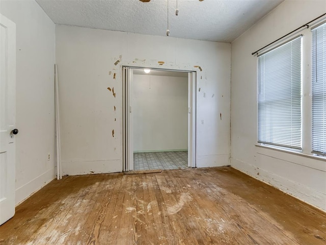 empty room with ceiling fan, light wood-type flooring, and a textured ceiling