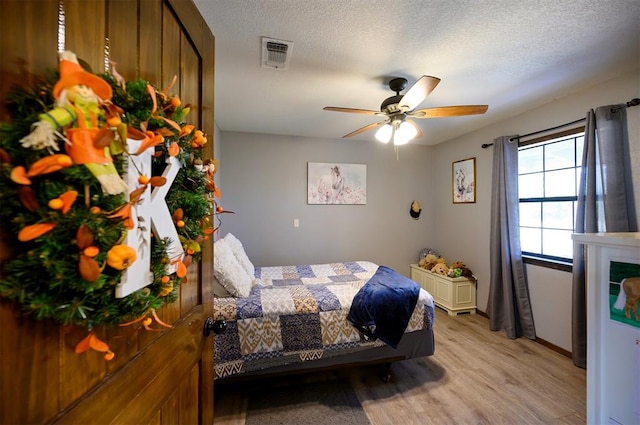 bedroom with ceiling fan, a textured ceiling, and light hardwood / wood-style flooring