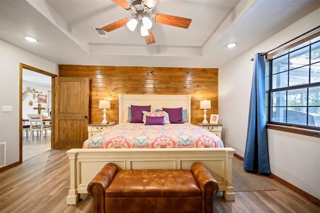 bedroom featuring hardwood / wood-style floors, ceiling fan, wood walls, and a raised ceiling