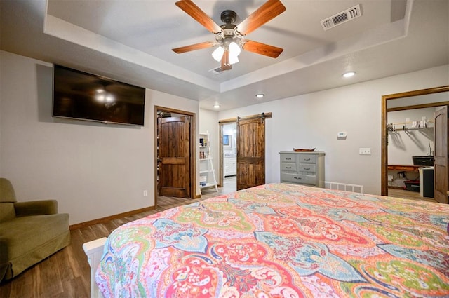 bedroom featuring hardwood / wood-style floors, ceiling fan, a barn door, and a raised ceiling