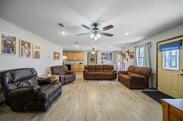 living room featuring a textured ceiling, light hardwood / wood-style floors, and ceiling fan