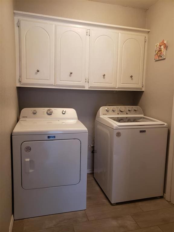 laundry area with washer and dryer, wood-type flooring, and cabinets