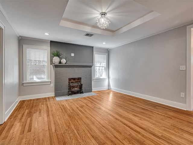 unfurnished living room featuring a wood stove, a raised ceiling, light hardwood / wood-style flooring, crown molding, and a chandelier