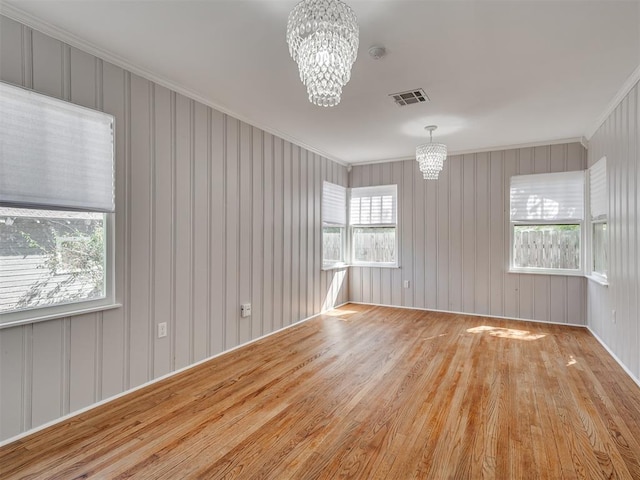 unfurnished room featuring a notable chandelier, light wood-type flooring, and ornamental molding