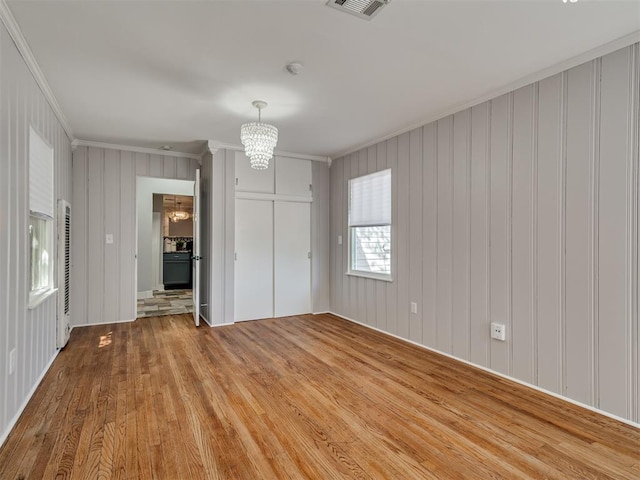 unfurnished bedroom with hardwood / wood-style flooring, a notable chandelier, and crown molding