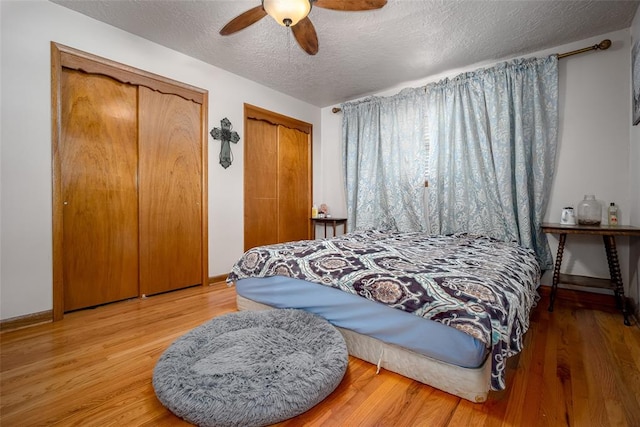 bedroom with multiple closets, ceiling fan, wood-type flooring, and a textured ceiling