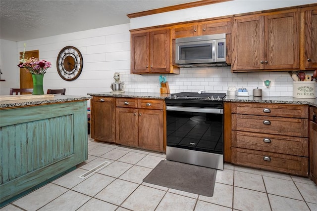 kitchen with stainless steel appliances, tasteful backsplash, light stone counters, wood walls, and light tile patterned floors