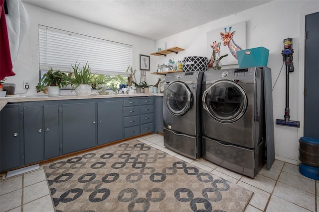 clothes washing area with cabinets, a textured ceiling, washer and clothes dryer, and light tile patterned flooring