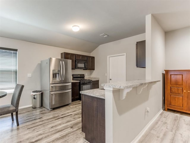 kitchen featuring lofted ceiling, black appliances, light hardwood / wood-style floors, a kitchen bar, and kitchen peninsula