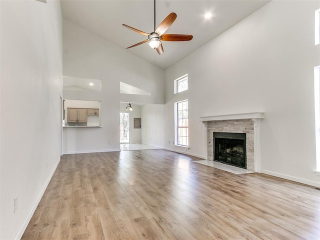 unfurnished living room featuring a fireplace, ceiling fan, light hardwood / wood-style flooring, and high vaulted ceiling