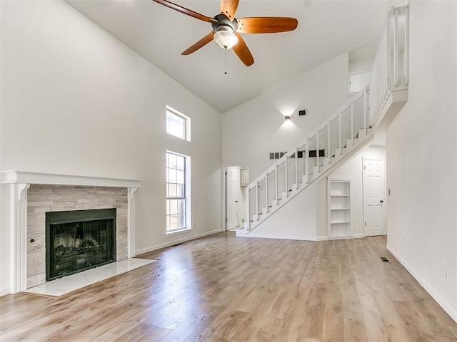 unfurnished living room featuring a tile fireplace, ceiling fan, light hardwood / wood-style flooring, and high vaulted ceiling