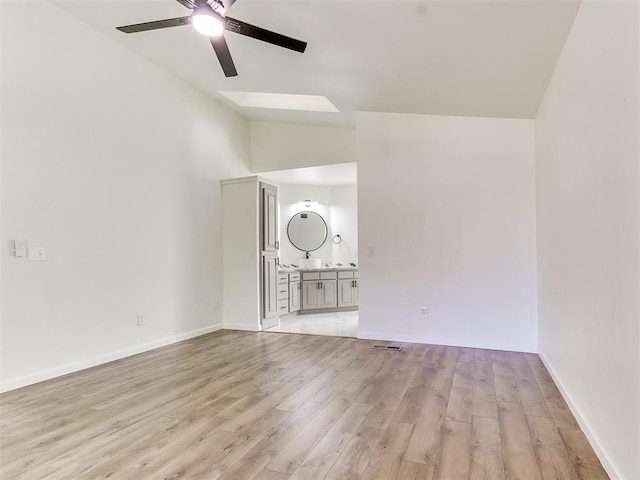 unfurnished living room with light wood-type flooring, ceiling fan, and vaulted ceiling with skylight