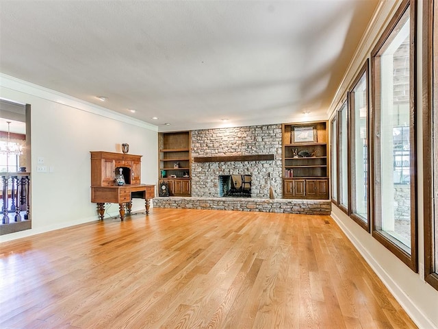 living room with built in features, a stone fireplace, light wood-type flooring, and a wealth of natural light