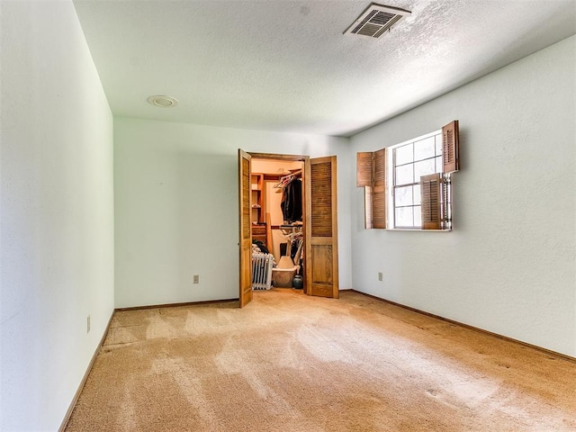 unfurnished bedroom with light colored carpet, a walk in closet, a textured ceiling, and a closet