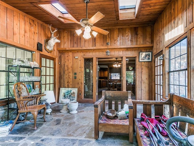 interior space with a skylight, ceiling fan, wooden ceiling, a high ceiling, and wood walls