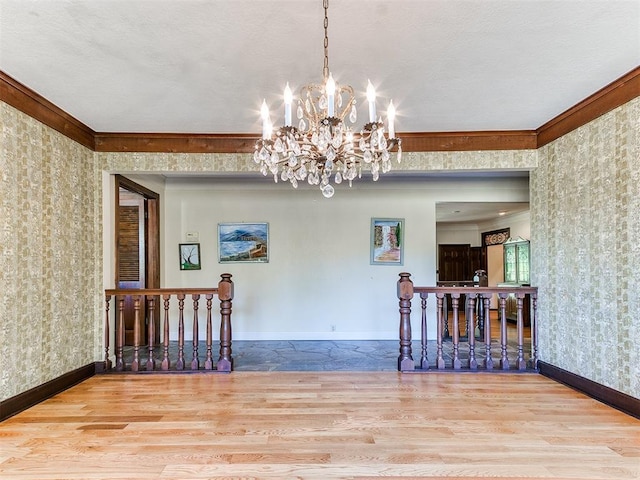 spare room featuring an inviting chandelier, ornamental molding, and light wood-type flooring