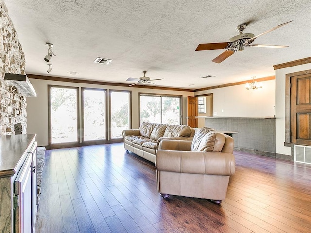 living room with dark hardwood / wood-style floors, a stone fireplace, crown molding, and a textured ceiling